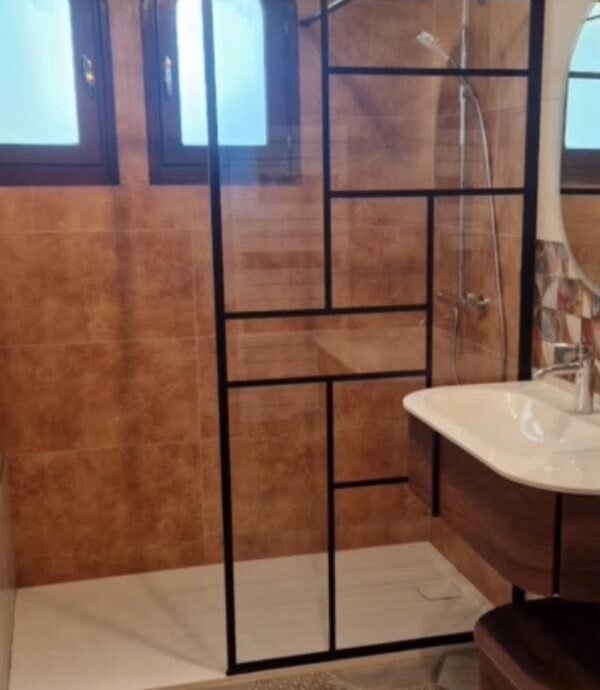 Après : salle de bain refaite avec paroi vitrée à cadre noir et sol de carreaux hexagonaux