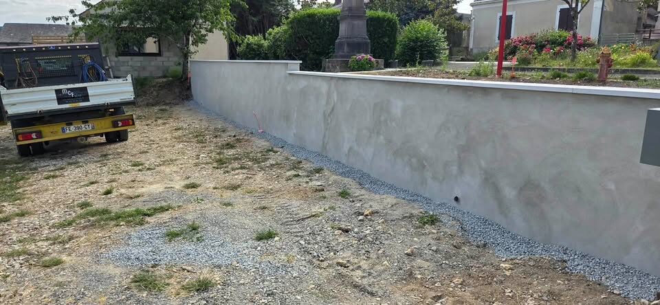 Mur de clôture enduit en gris, longeant une cour gravillonnée