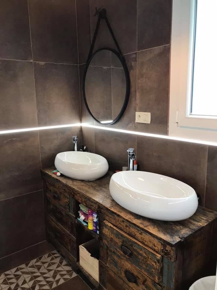 Salle de bain avec double vasque, murs en carreaux sombres et miroir rond