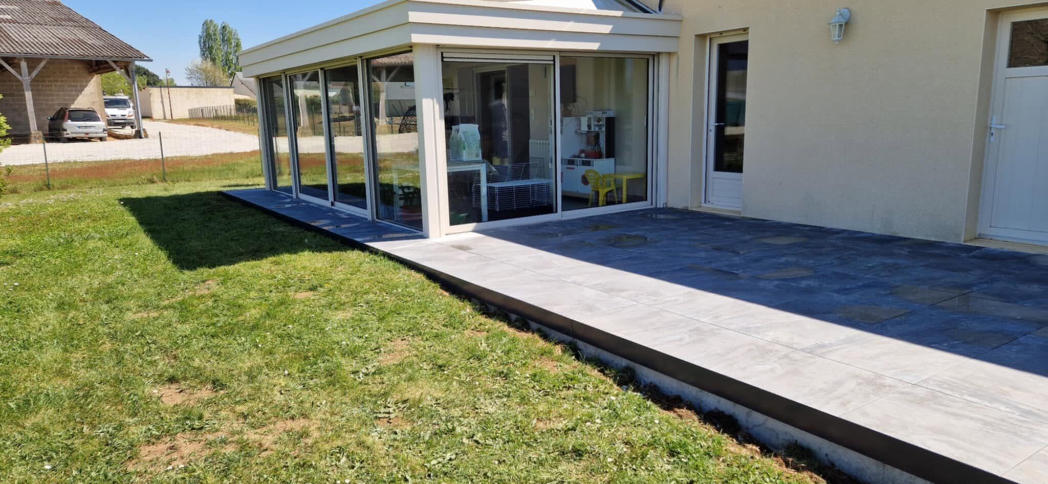 Terrasse en dalles grises le long d'une véranda, bordure claire